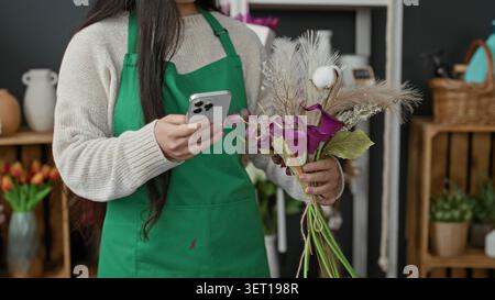 Woman florist holds smartphone in hand while arranging a purple calla lilies bouquet and pampas grass in a studio; calm focus. Stock Photo