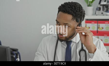 Man doctor with stethoscope rubs neck while adjusting headset in building during virtual consult; concern. Stock Photo