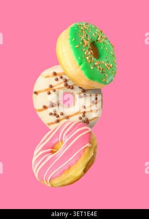 Yummy donuts covered with icing falling on pink background Stock Photo