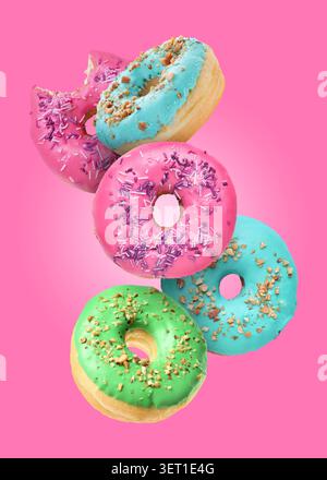Tasty donuts covered with icing falling on pink background Stock Photo