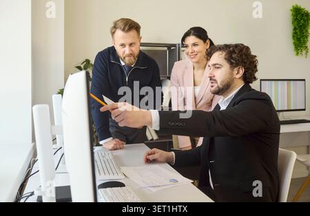 Team of colleagues discussing project data at computer in office strategy meeting Stock Photo