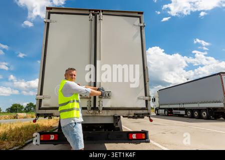 Delivery courier in a safety vest opening the back cargo doors of a white commercial box truck Stock Photo