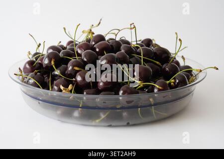 Fresh dark sweet cherries piled in a clear plastic bowl on a clean white background Stock Photo