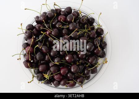 Top view of fresh dark sweet cherries with stems in a clear plastic bowl on a white background Stock Photo