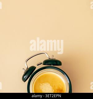 Cup of fresh espresso integrated into a retro alarm clock on beige background. Creative coffee concept. Morning routine, wake up time idea. Stock Photo
