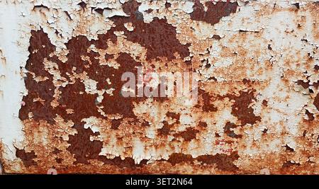 Rust spreads over a weathered metal surface in an industrial area, showing layers of peeling paint and corrosion in bright daylight Stock Photo