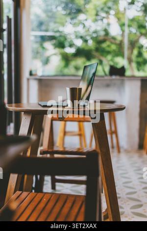 Cozy café corner in Bangkok, Thailand — wooden table with laptop and metal cup, soft natural light Stock Photo