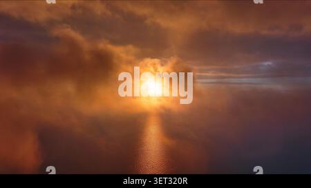 Moving in clouds to bright sun setting over calm sea Stock Photo