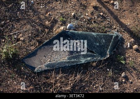 Broken glass lies scattered on dry earth. Rough terrain surrounds shattered surface when close to a rest stop whilst crossing the Nullarbor Plain Stock Photo