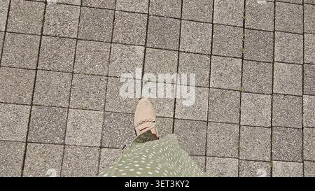 A view from above showing a person's feet in shoes walking on a paved stone surface. Stock Photo