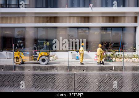 Construction workers in yellow uniforms working with a Sakai road roller vehicle on a sidewalk in Okinawa, Japan. Stock Photo
