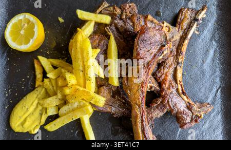 Greek-style grilled lamb chops (Païdakia), seasoned with lemon, oregano, and garlic. Crispy fries as a side seasoned with herbs Stock Photo