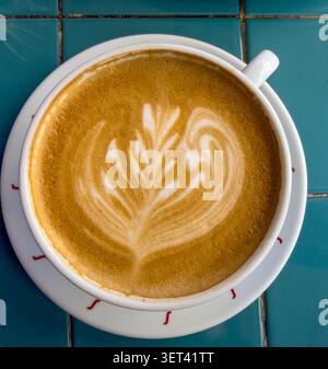 Hot cup of coffee with fern latte art in a white cup on the green table Stock Photo