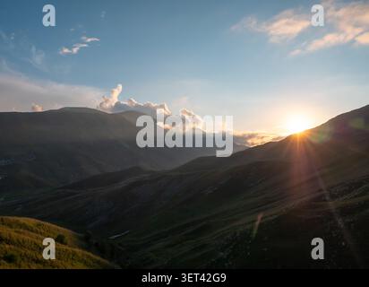 Majestic sunset over mountain ranges with dramatic clouds and warm light in the evening sky Stock Photo
