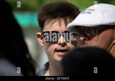 Young Cuban man with Down syndrome wearing sunglasses standing in a crowd during a community social project in Ciego de Avila, Cuba Stock Photo
