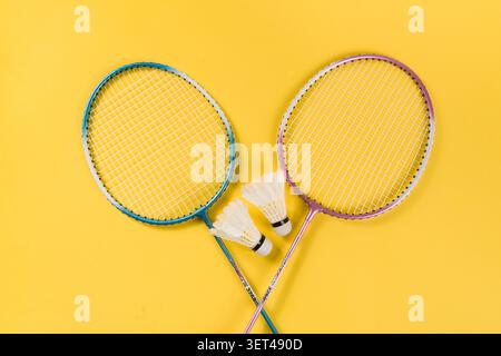 Two badminton rackets and shuttlecocks displayed on a vibrant yellow background Stock Photo