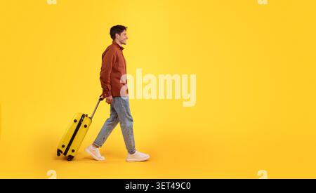 Young Man Walking With Yellow Luggage On Yellow Background, Travel Concept Stock Photo