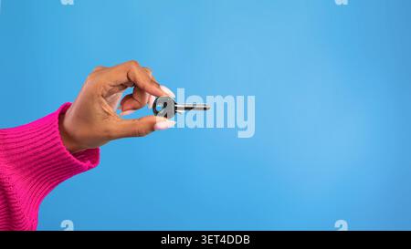 Hand Holding Silver Key Against Blue Background, Unrecognizable Person, Security Concept Stock Photo