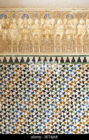 Intricate Arabic carved stucco decoration and colorful geometric ceramic tiles on a historic wall at the Alhambra palace complex in Granada, Spain Stock Photo