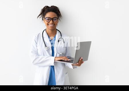 Smiling African American Female Doctor Using Laptop In Clinic, Healthcare Concept Stock Photo