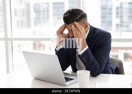 Frustrated businessman sits at desk with laptop Stock Photo