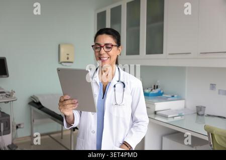 Happy mature GP doctor woman watching content on tablet Stock Photo