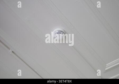 Smoke detector mounted on white ceiling in indoor space Stock Photo