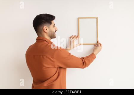 Young Man Holding Empty Picture Frame, Preparing To Hang On Wall, Home Decor Concept Stock Photo