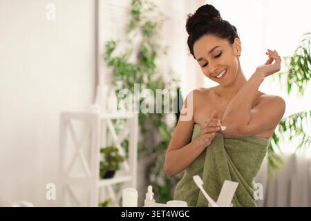 Happy Young Woman Applying Moisturizer At Home Bathroom, Skincare Routine Stock Photo