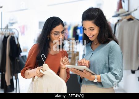 Boutique workers engaged in discussion, reviewing inventory using tablet Stock Photo