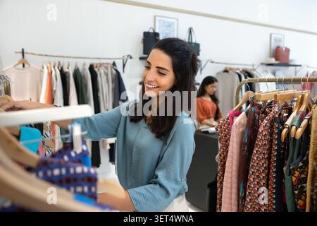 Smiling Brazilian woman browsing clothes in modern boutique store Stock Photo