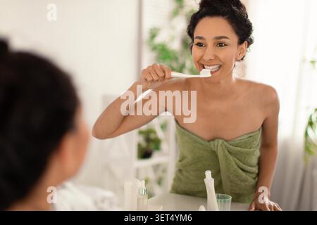 Young African American Woman Brushing Teeth In Bathroom, Smiling, Self-care Concept Stock Photo