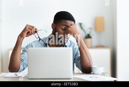 Tired african american employee having headache after working on laptop Stock Photo