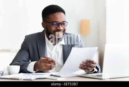 Cheerful black businessman checking reports and making notes Stock Photo