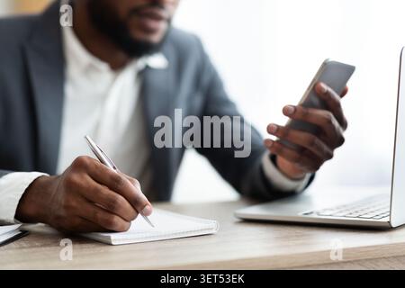 African American employer using smartphone and taking notes in office Stock Photo