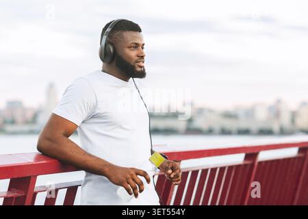 Dreamy black athletic guy resting on city bridge Stock Photo