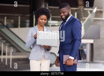 Young woman pointing finger to laptop screen while standing outdoors Stock Photo