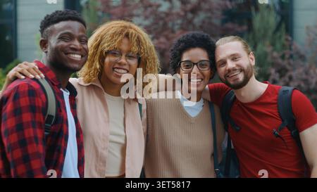 Group of four multiracial students laughing happy hugging looking at camera in city multiethnic friends candid humorous having fun smiling laugh hug Stock Photo