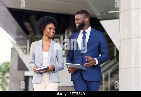 Two smiling african coworkers walking outdoors together Stock Photo