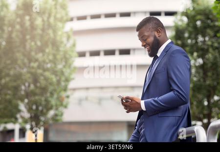 Attractive businessman texting on cellphone, standing near modern office building Stock Photo