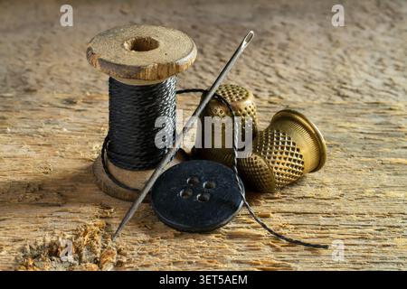 Old sewing utensils on the background of wood. A spool of thread, a button, a needle, thimbles. Stock Photo