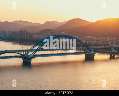 Stunning aerial view of a bustling bridge with cars traversing over a serene river during sunset. Hangzhou, China. Stock Photo
