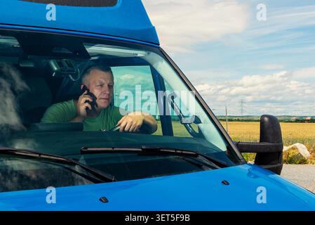 Side view of a professional driver speaking on smartphone while driving a commercial blue van Stock Photo