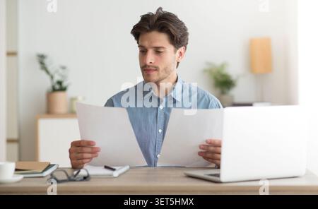 Man Reading Documents at a Desk in a Bright Modern Office Setting Stock Photo