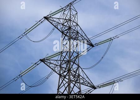 Close‑up of a high‑voltage electricity pylon near the River Lee, showing glass insulators and power lines against a bright blue sky. Stock Photo