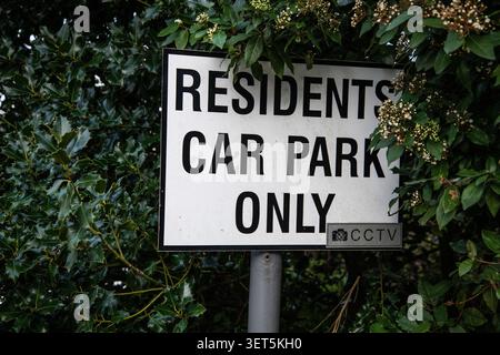 Close‑up of a “Residents Car Park Only” sign with CCTV symbol surrounded by dense green foliage, representing private parking and security enforcement Stock Photo