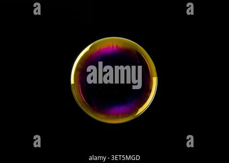 Soap bubble displaying vibrant iridescent colors and reflections against a dark background Stock Photo