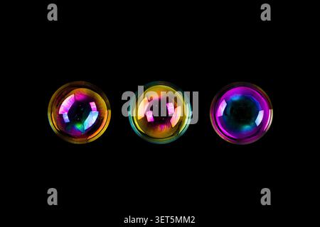 Three colorful iridescent soap bubbles floating against a dark black background Stock Photo