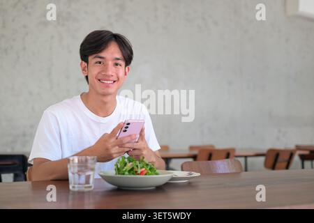 Horizontal lifestyle photograph of a handsome young Southeast Asian Thai Isan non-binary man smiling happily and looking directly at the camera while Stock Photo