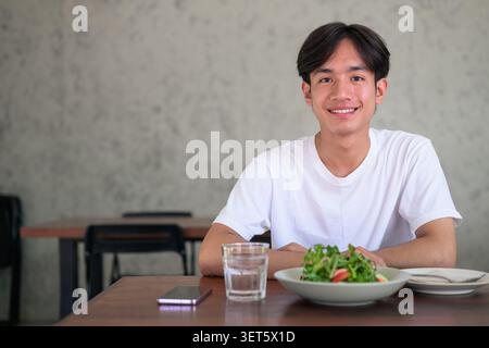 Horizontal lifestyle photograph of a handsome young Southeast Asian Thai Isan non-binary man smiling happily and looking directly at the camera while Stock Photo